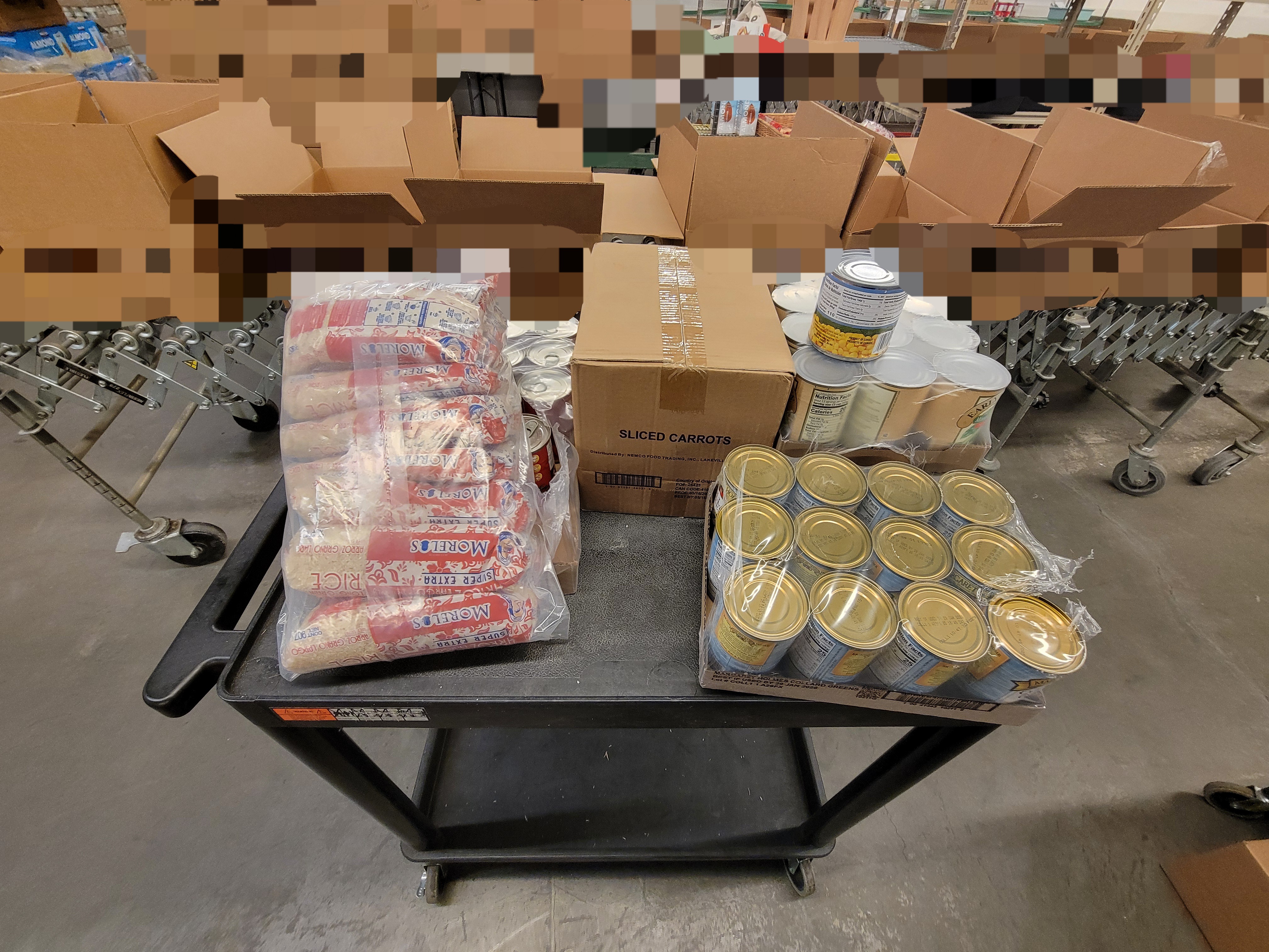 Food filled shelf cart with box filled conveyor belt behind it.